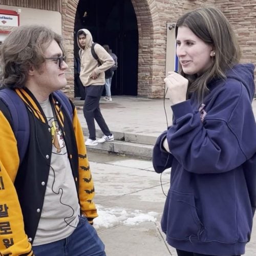 Person with long brown hair and navy sweatshirt talking to person with long brown hair and varsity jacket.